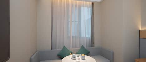A modern hotel room with a light blue sofa, a round wooden table, and a large window with sheer curtains.