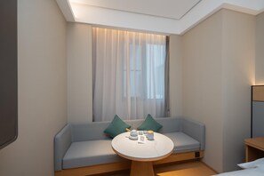 A modern hotel room with a light blue sofa, a round wooden table, and a large window with sheer curtains. - Ji Hotel Guangzhou Panyu Chimelong Wanbo (Guangzhou)