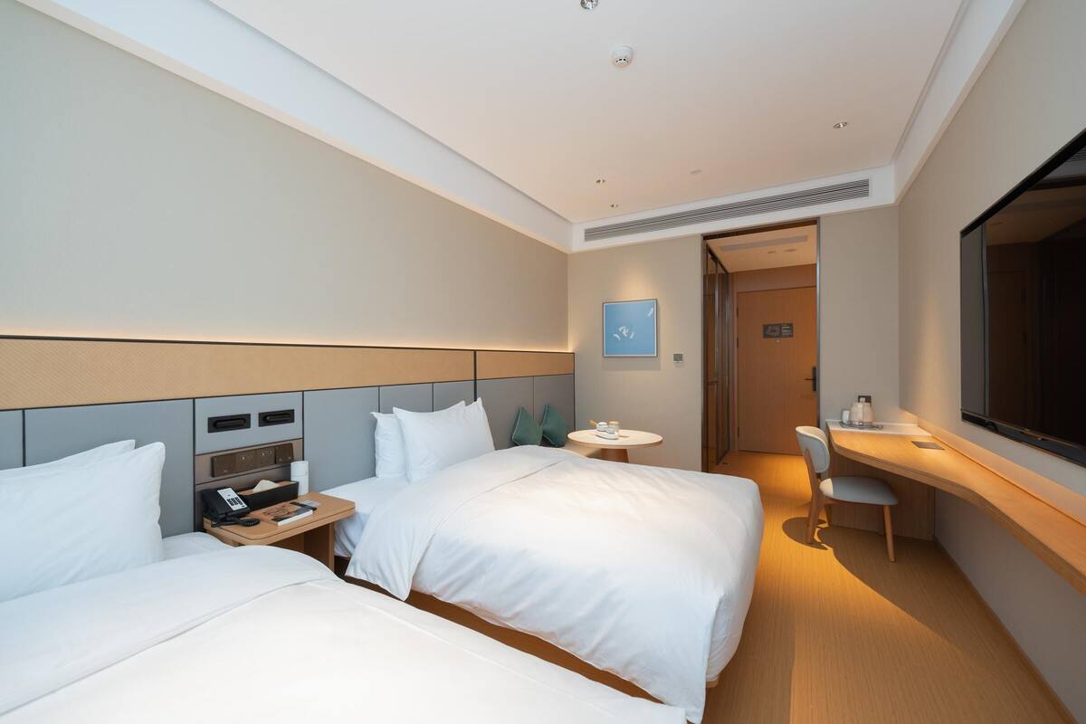A hotel room with two beds, a desk, a chair, and a small table.