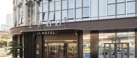 Une entrée d’hôtel moderne avec une façade en verre, une enseigne indiquant « JI HOTEL » et une porte tournante.