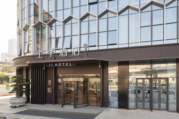 A modern hotel entrance with a glass facade, a sign reading "JI HOTEL", and a revolving door.