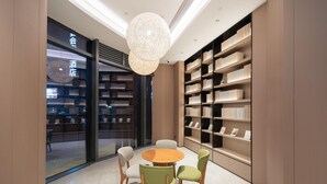 A modern interior with a round wooden table surrounded by chairs, a large bookshelf, and a hanging light fixture. - Ji Hotel Guangzhou Panyu Chimelong Wanbo (Guangzhou)