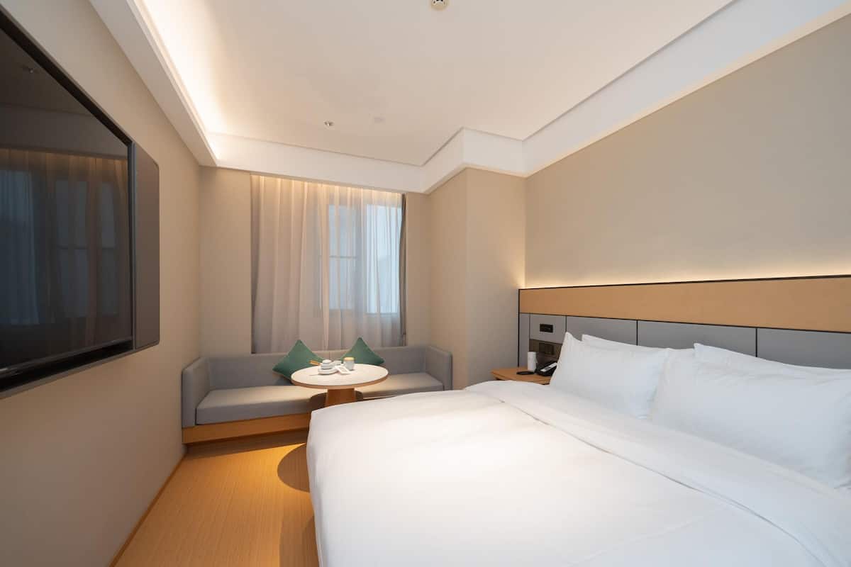 A hotel room with a large bed, a small sofa, a round table, and a large mirror.