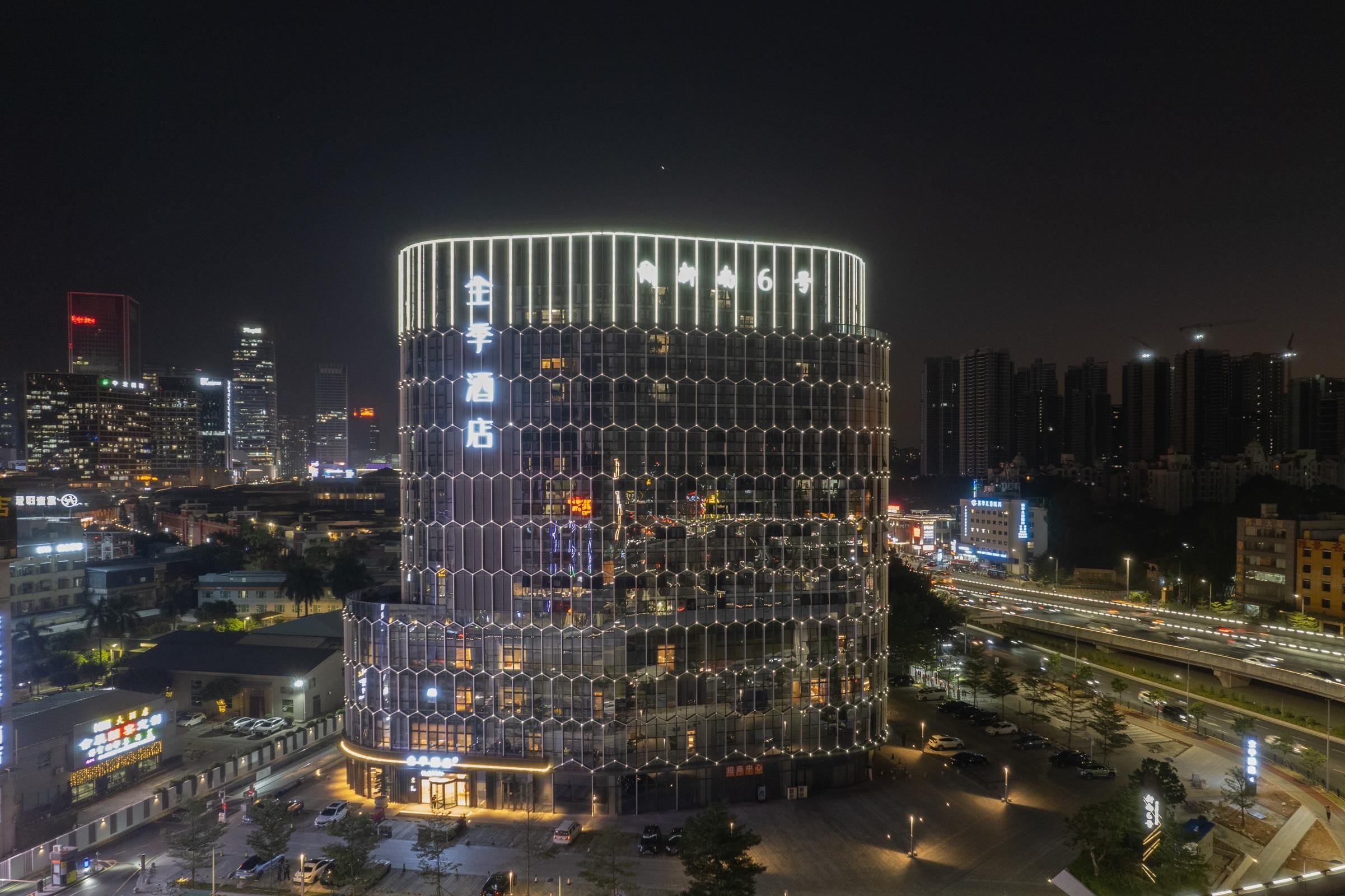 A modern hotel with a distinctive hexagonal facade and a circular design, surrounded by a busy urban environment at night.