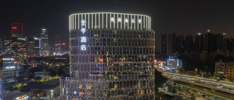 A modern hotel with a distinctive hexagonal facade and a circular design, surrounded by a busy urban environment at night.