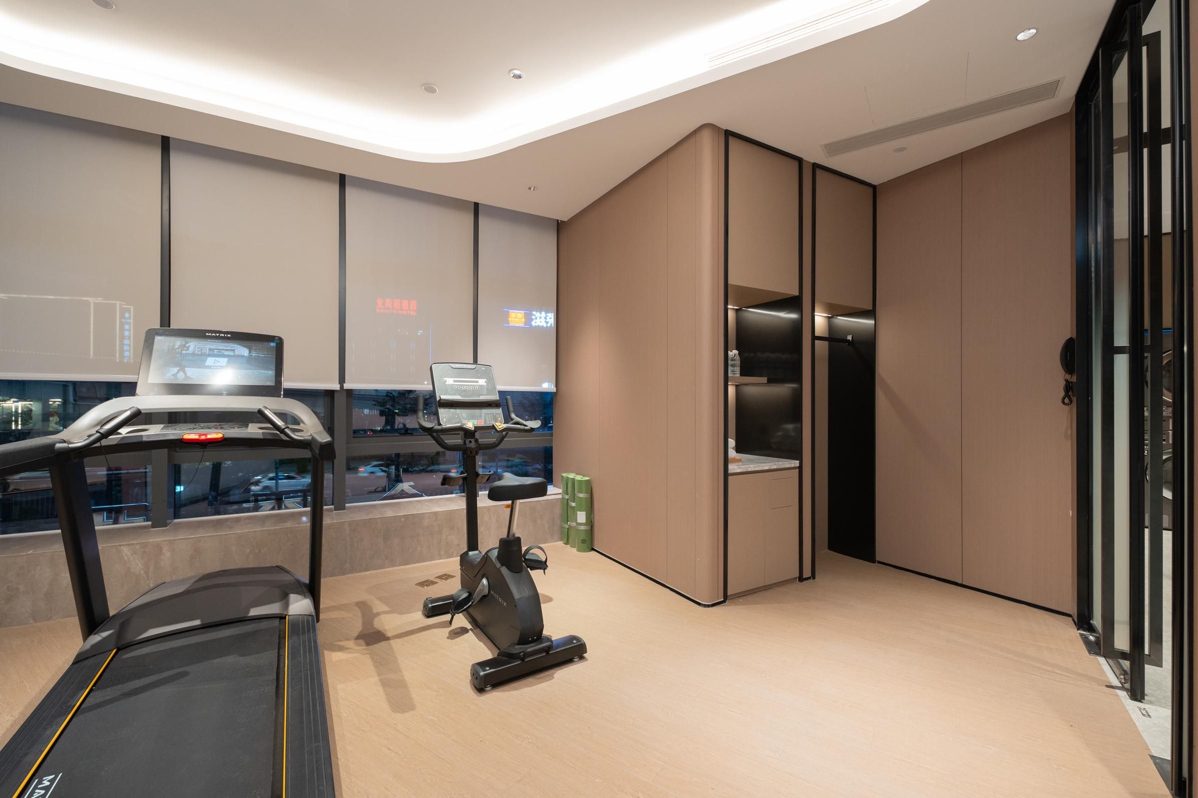 Een moderne hotelkamer met een loopband, een hometrainer en een groot raam met uitzicht op de stad.