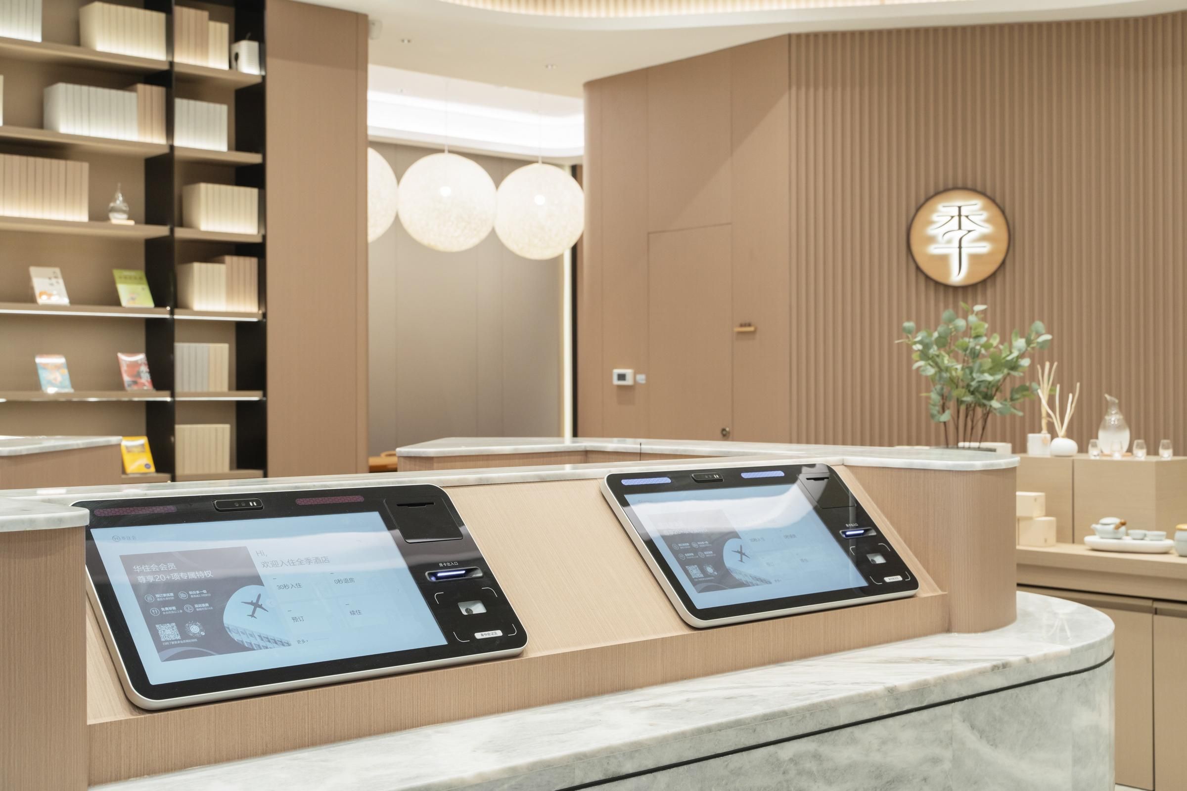 Un mostrador de recepción moderno con pantallas digitales, una zona de espera de madera y un letrero en la pared.