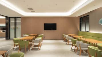 Un comedor moderno con varias mesas y sillas, un televisor de pantalla plana en la pared y una puerta de cristal que da a la cocina.