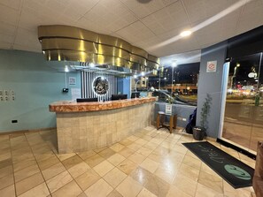 A reception area with a marble counter, a decorative wall with a circular emblem, and a view of the street outside. - Hotel Italia Cuenca (Cuenca)