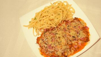 Une assiette de spaghettis accompagnée d’un plat à base de viande, peut-être du poulet parmesan, le tout servi dans une assiette blanche.