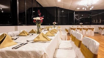 A banquet hall with long tables, gold sashes, and white tablecloths.