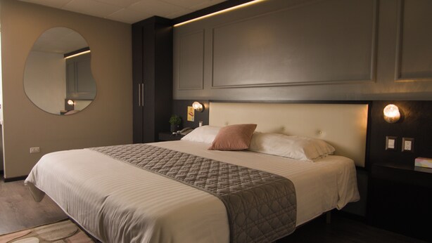 A neatly made bed with a quilted bedspread and pillows, a round mirror on the wall, and a nightstand with a lamp. - Hotel Italia Cuenca (Cuenca)