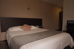 A hotel room with a bed, a pillow, a bedside table with a phone, and a wall-mounted light. - Hotel Italia Cuenca (Cuenca)