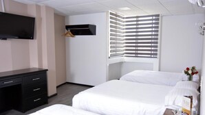 Camera d'hotel con un letto, una scrivania, una televisione, una finestra con persiane e una mensola a parete.