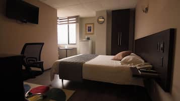Habitación de hotel con cama, escritorio, silla y televisor montado en la pared.
