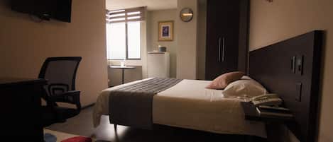 A hotel room with a bed, desk, chair, and a TV mounted on the wall.