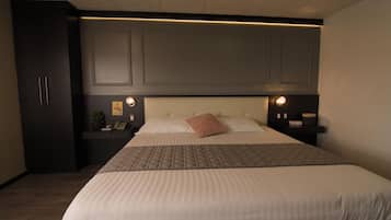 A hotel room with a large bed, a nightstand, a desk, and a wardrobe.