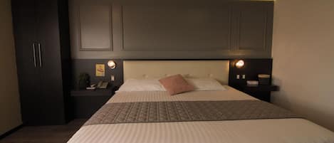 A hotel room with a large bed, a nightstand, a desk, and a wardrobe.