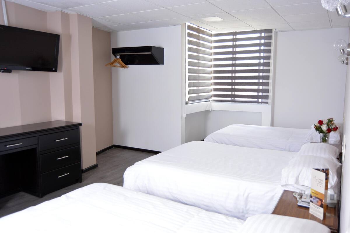 Une chambre d’hôtel avec deux lits, un bureau, une télévision et une fenêtre avec des stores.