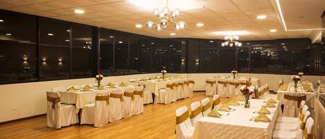 A banquet hall with round tables, white tablecloths, gold sashes, and a chandelier.