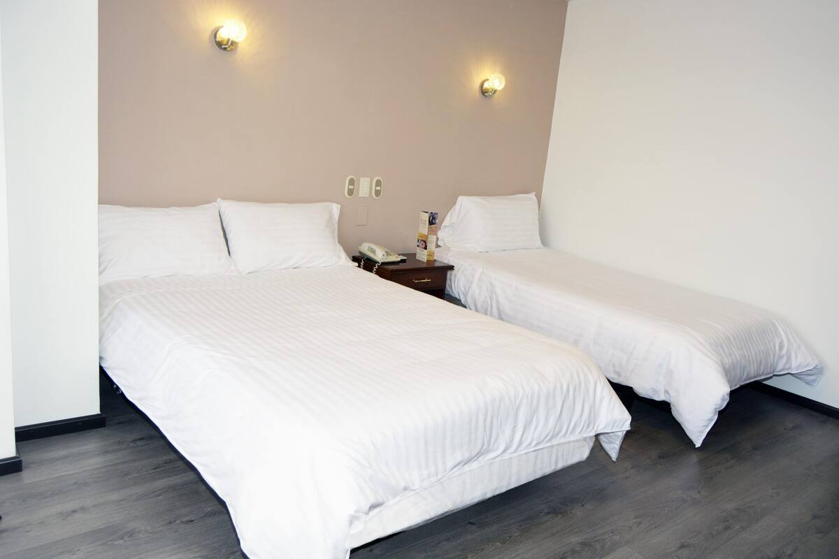 Une chambre d’hôtel avec deux lits simples, une table de chevet avec une lampe et un téléphone fixé au mur.