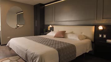 A neatly made bed with a quilted bedspread and pillows, a round mirror on the wall, and a nightstand with a lamp.