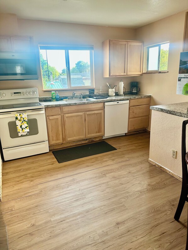 A kitchen with wooden cabinets, a white stove, a dishwasher, and a window providing natural light.