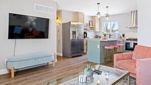 A modern living room with a flat-screen TV, a light blue sofa, a pink armchair, and a glass coffee table. - Completely Renovated Home in St. Charles, Missouri (Saint Charles)