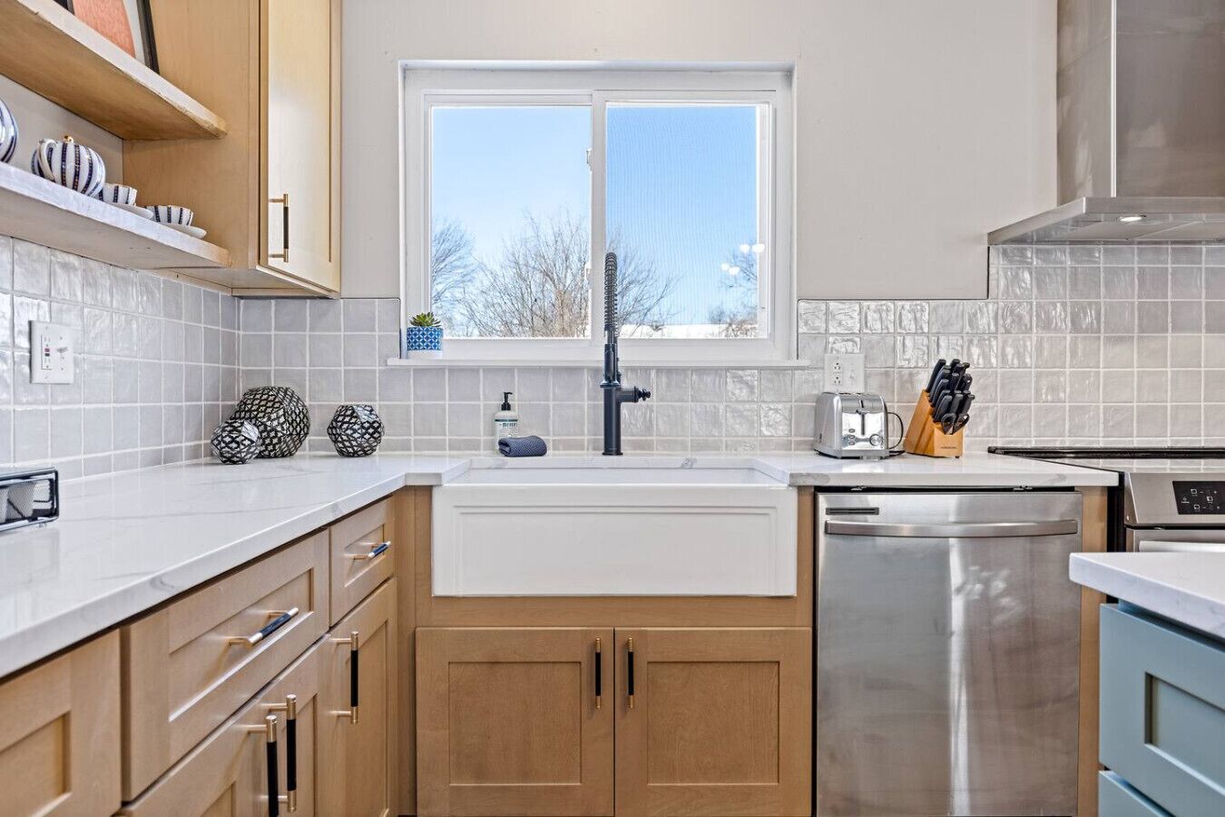 Een moderne keuken met houten kastjes, een RVS vaatwasser en een raam dat voor daglicht zorgt.