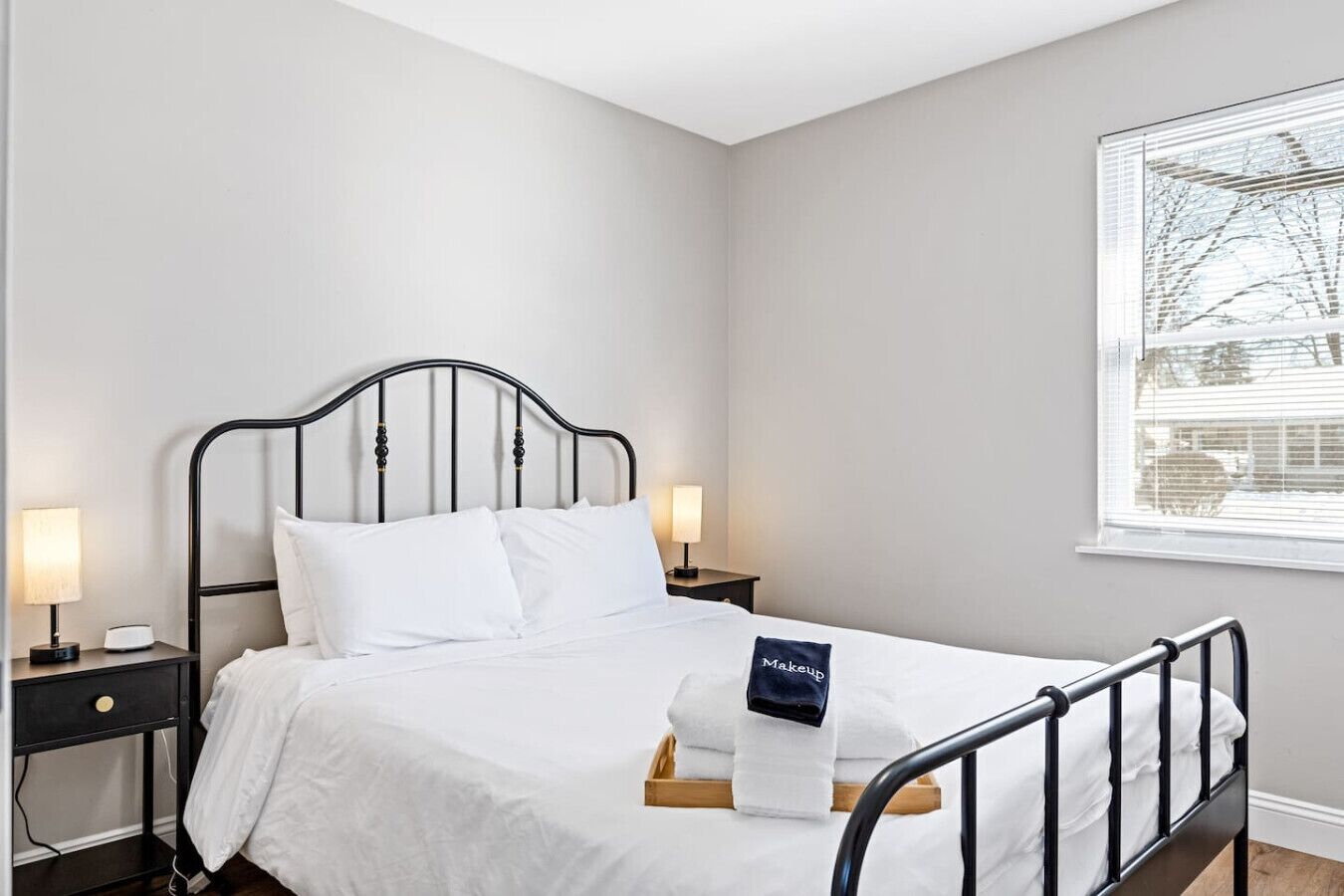Ein ordentlich gemachtes Bett mit weißen Leinen, einem schwarzen Metall-Kopfteil und einem Nachttisch mit einer Lampe.