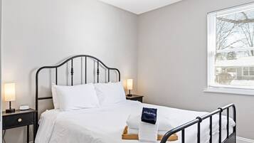 Ein ordentlich gemachtes Bett mit weißen Leinen, einem schwarzen Metall-Kopfteil und einem Nachttisch mit einer Lampe.