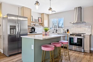 A modern kitchen with a stainless steel refrigerator, an island with pink stools, a gas stove, and a large window. - Completely Renovated Home in St. Charles, Missouri (Saint Charles)