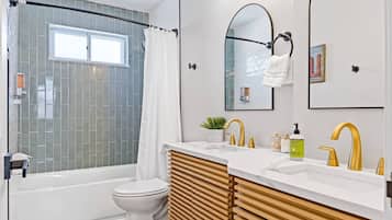 A modern bathroom with a bathtub, two sinks, a toilet, and a shower area.