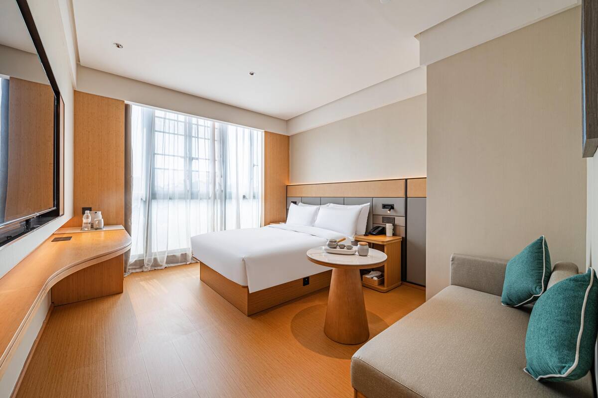 Ein modernes Hotelzimmer mit einem großen Bett, einer Couch, einem kleinen Tisch und einem Fernseher.