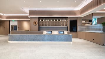 Een moderne hotel receptie met een marmeren balie, digitale schermen en een traditionele Aziatische wand met een cirkelvormig symbool.