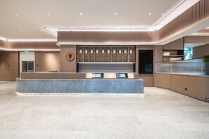 A modern hotel reception area with a marble counter, digital displays, and a traditional Asian-style wall with a circular emblem. - Ji Hotel Guangzhou Panyu Shiqiao Metro Station (Guangzhou)