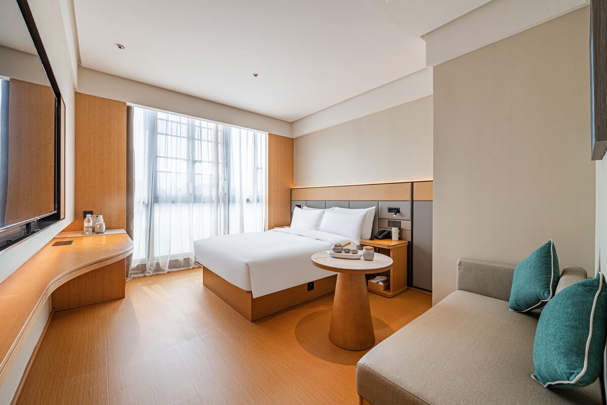 A modern hotel room with a large bed, a sofa, a small table, and a TV.