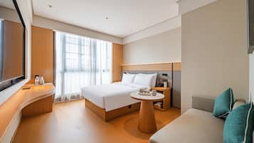A modern hotel room with a large bed, a sofa, a small table, and a TV.