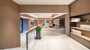 Un moderno hall de hotel con una recepción central, un panel de vidrio y una planta.