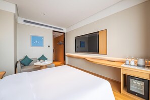 A hotel room with a bed, a small table with a cup and a remote, a TV on a stand, a mini-fridge, and a coat rack. - Ji Hotel Guangzhou Panyu Shiqiao Metro Station (Guangzhou)