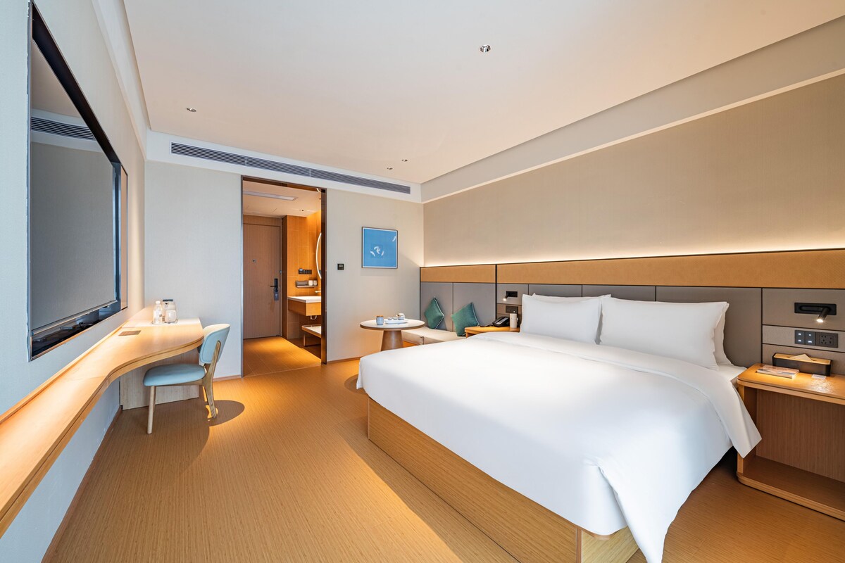 A modern hotel room with a large bed, a desk, and a chair.