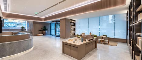 A modern hotel lobby with a curved reception desk, a central seating area, and large windows offering a view of the city.