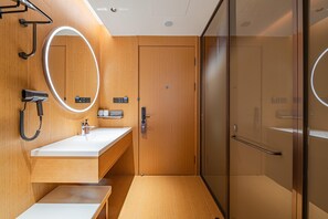A modern bathroom with a wooden vanity, a mirror with lights, a hairdryer, and a glass shower enclosure. - Ji Hotel Guangzhou Panyu Shiqiao Metro Station (Guangzhou)