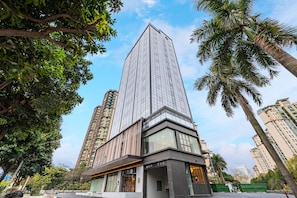 A modern high-rise building with a glass facade, surrounded by palm trees and other greenery. - Ji Hotel Guangzhou Panyu Shiqiao Metro Station (Guangzhou)