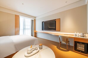 A hotel room with a bed, a desk with a television, a coffee machine, and a minibar.