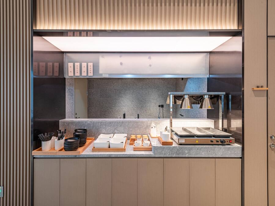 A modern kitchen with a stainless steel range hood, a marble countertop, and neatly arranged utensils and dishes.
