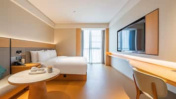 A modern hotel room with a bed, bedside table, and a desk with a chair.