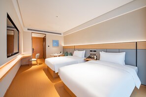 Ein Hotelzimmer mit zwei Betten, einem Schreibtisch, einem Stuhl und einem großen Spiegel.