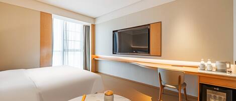 Une chambre d’hôtel équipée d’un lit, d’un bureau avec une télévision, d’une machine à café et d’un mini-bar.