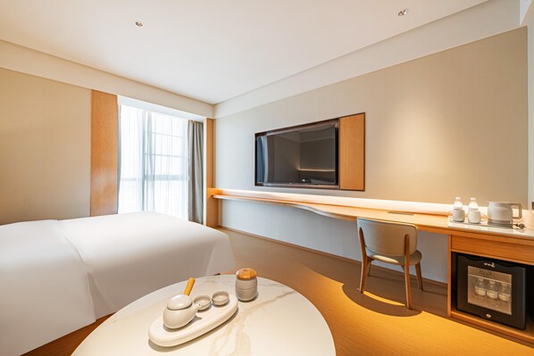 A hotel room with a bed, a desk with a television, a coffee machine, and a minibar. - Ji Hotel Guangzhou Panyu Shiqiao Metro Station (Guangzhou)